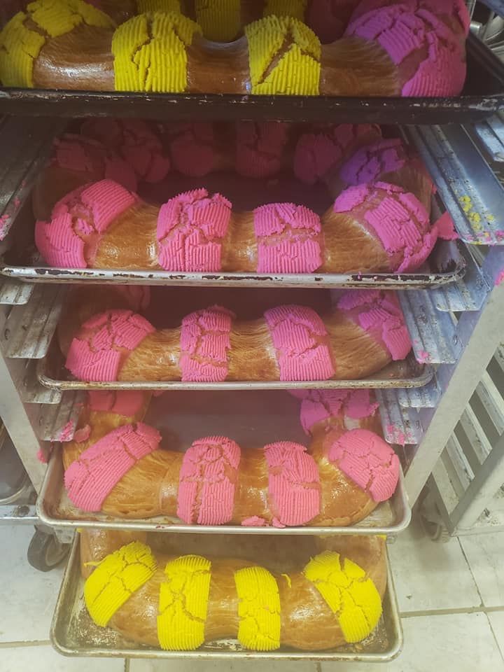 Racks of rosca de reyes with pink and yellow topping, fresh from the La Popular ovens